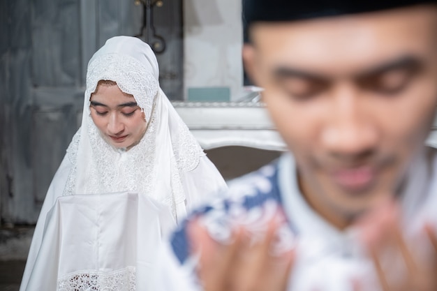 Asian muslim husband and wife praying jamaah together at\
home