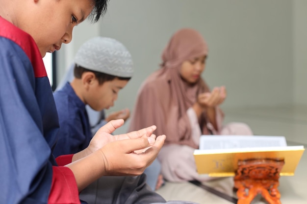 Asian muslim kids praying dua after or before reading Quran together with multiethnic friends