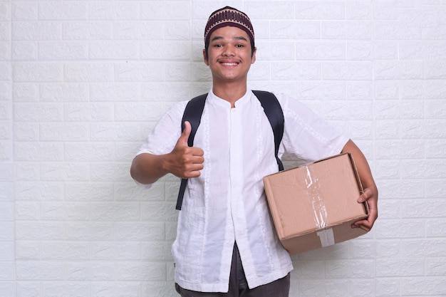 Asian Muslim man carrying box while giving thumb up ready to travel back to hometown to celebrate E