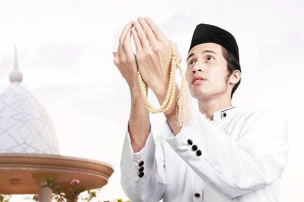 Asian Muslim man praying with prayer beads on his hands