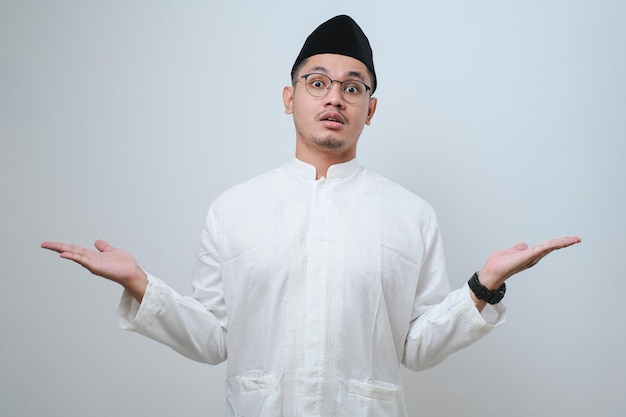 Asian muslim man raised arms and looking at camera with doubtful face studio shot isolated on light grey background