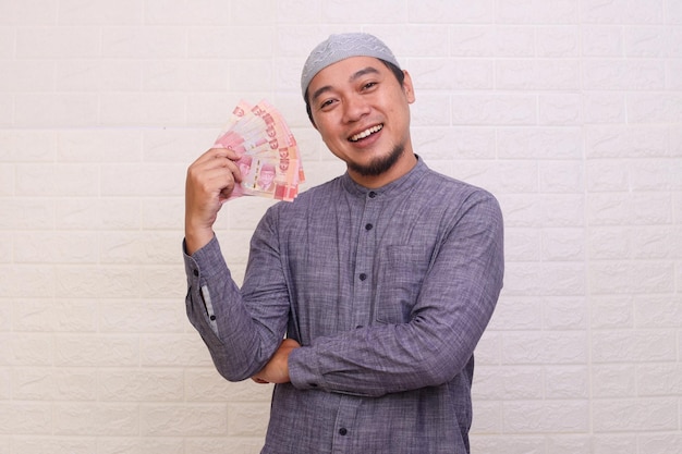 Asian Muslim man showing cash money in Indonesian rupiah banknotes isolated over white background