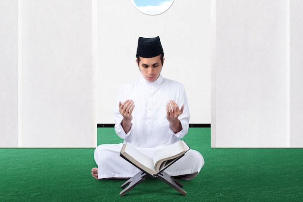 Asian Muslim man sitting while raised hands and praying on the mosque