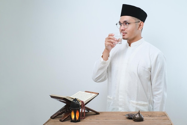 Asian muslim man smiling and thumbs up while going to drink a glass of water for break fasting over white background