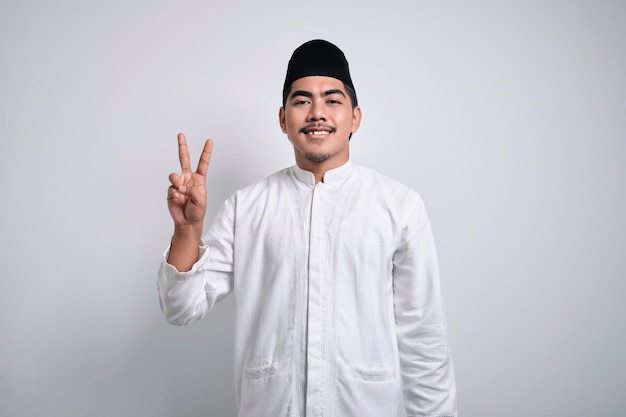 写真 カジュアルな服を着たアジアのイスラム教徒の男性が、自信を持って幸せな笑顔を見せながら、2番の指で上向きを示しています