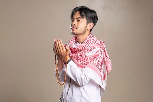 Foto uomo musulmano asiatico che indossa kufiya mentre prega alzando le mani