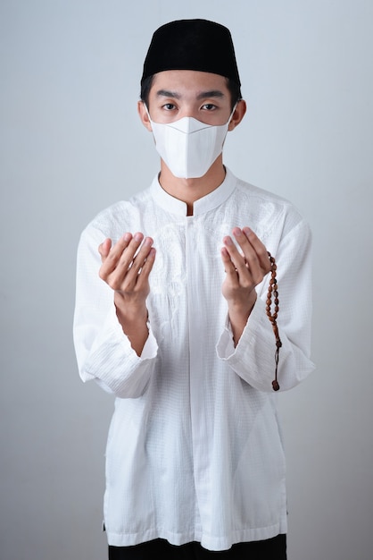 Foto uomo musulmano asiatico che indossa vestiti musulmani che tengono i grani di preghiera con la mascherina medica