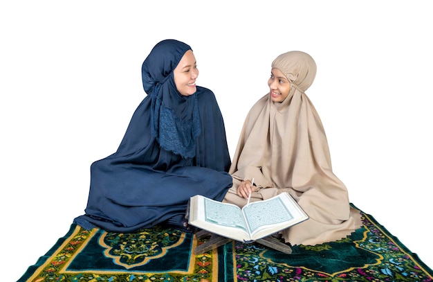 Asian Muslim mother and daughter in a hijab on a prayer rug reading the Quran