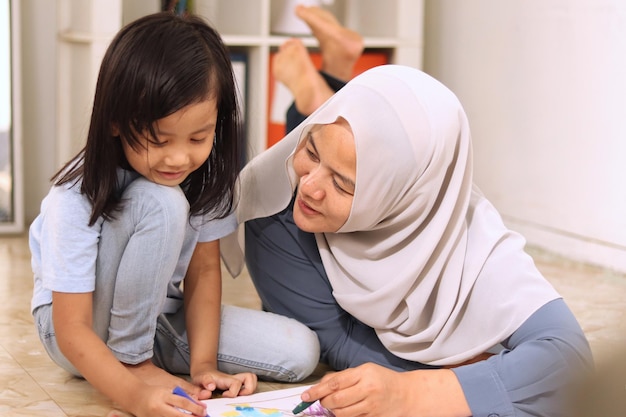 Asian muslim mother drawing with her daughter single mom teaching baby girl learning on the floor