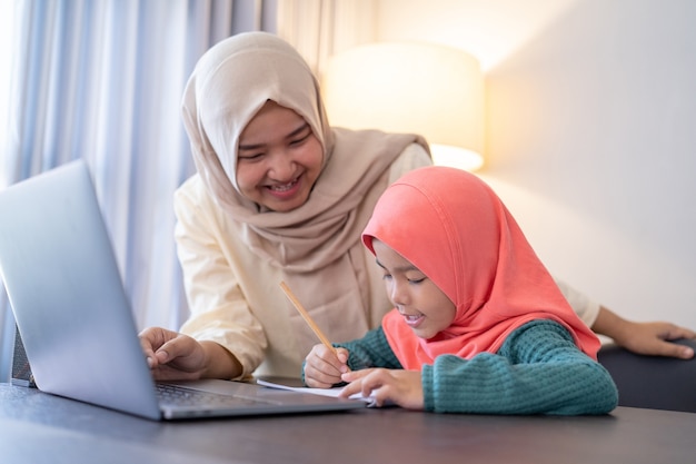 Asian muslim mother help her daughter to study during home schooling in the evening