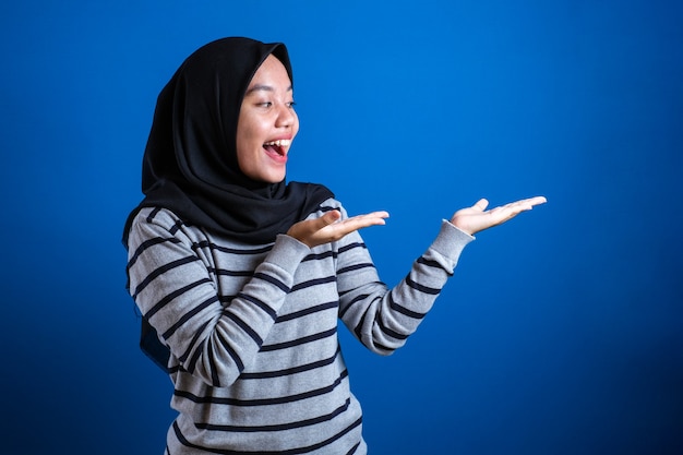 asian muslim student girl smiling and pointing to presenting something on her side with copy space