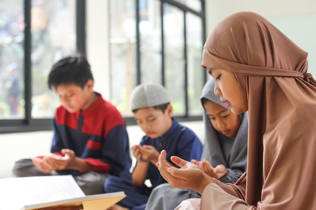 아시아 무슬림 십대 소녀가 다민족 친구들과 함께 코란을 읽은 후 또는 전에 두아를 기도하고 있습니다.