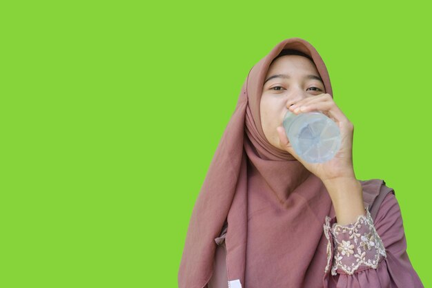 緑色の背景でボトル入りの水を飲むアジアのイスラム教徒の女性