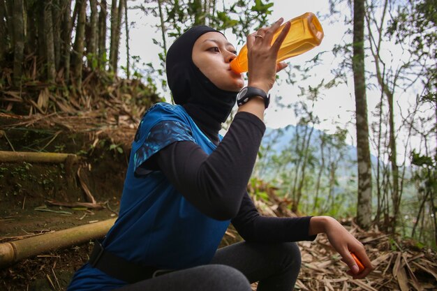 ジョギング、健康、スポーツのコンセプトの後に水を飲むアジアのイスラム教徒の女性。