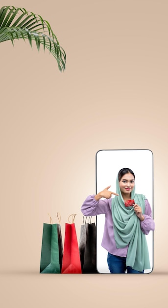 Asian Muslim woman in a headscarf holding a credit card on a mobile phone screen