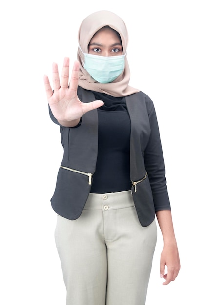 Asian Muslim woman in a headscarf and wearing a face mask showing a stop sign isolated over white background