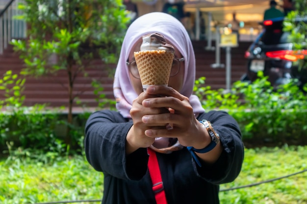 An Asian Muslim woman holding an ice cream cone with both hands Outdoors