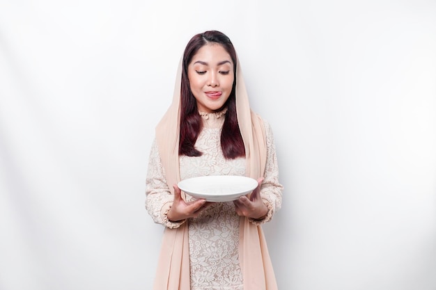 An Asian Muslim woman is fasting and hungry and holding utensils cutlery while looking aside thinking about what to eat