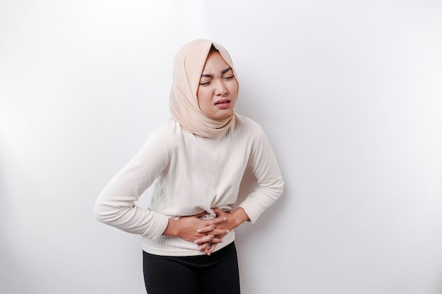 An Asian Muslim woman is fasting and hungry and touching her belly while looking aside thinking about what to eat