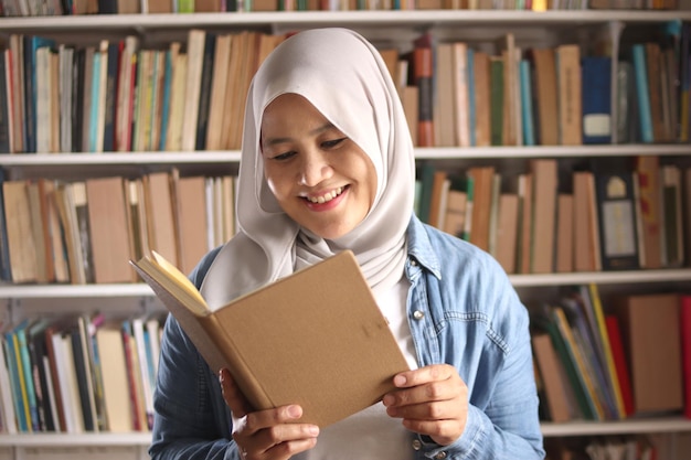 Foto donna musulmana asiatica che legge un libro in biblioteca concetto educativo espressione sorridente felice