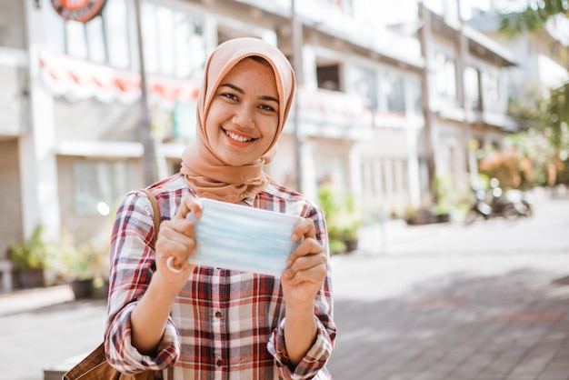 屋外に立っている間マスクを示すアジアのイスラム教徒の女性