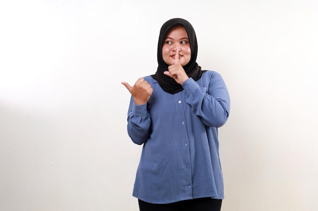 Asian muslim woman showing something beside her while making secret gesture