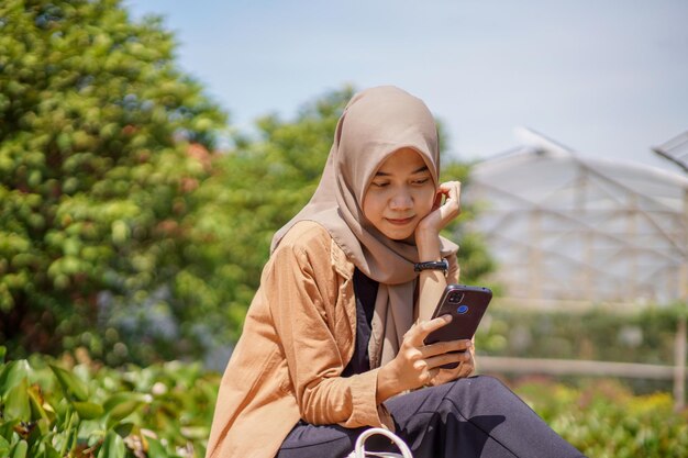 Photo asian muslim woman sitting and playing social media using her smartphone