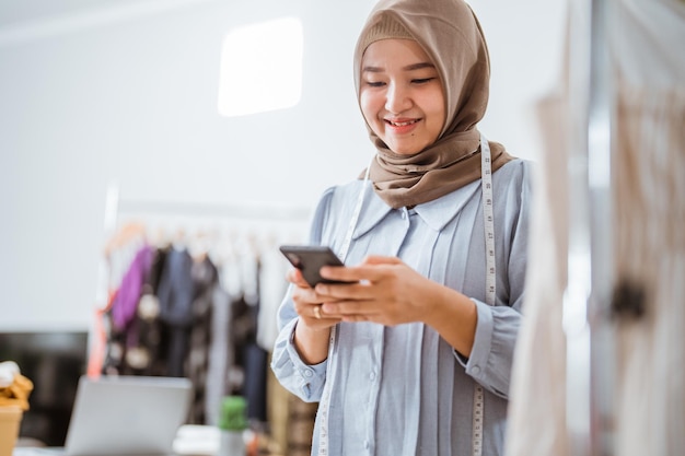 asian muslim woman small business owner at her shop selling through e commerce marketplace using her mobile phone