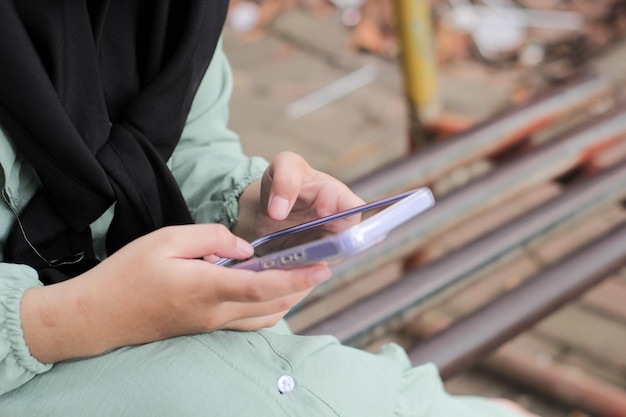 Foto donna musulmana asiatica che utilizza smartphone nel parco, primo piano delle mani