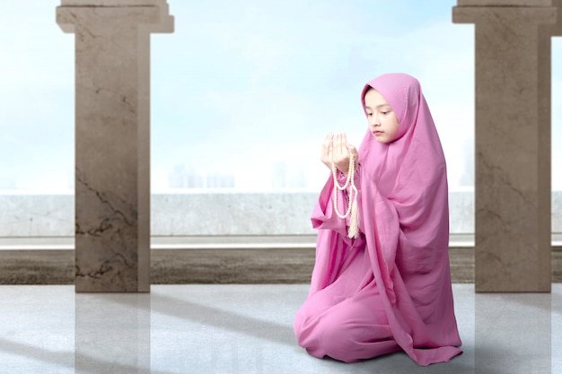 Asian Muslim woman in veil sitting and praying with prayer beads on her hands