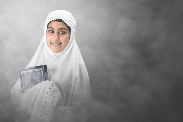 Asian muslim woman in a veil standing and holding the quran\
with bright background