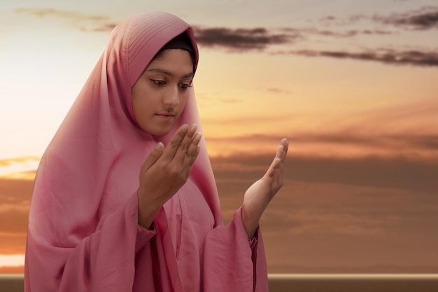 Asian Muslim woman in a veil standing while raised hands and praying