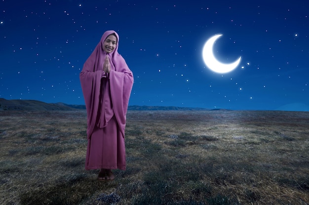 Asian muslim woman in veil with greeting gesture with the night\
scene background