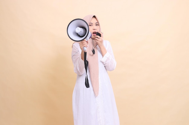 Asian Muslim woman wearing a hijab shouts at the camera sullenly holding a loudspeaker megaphone and