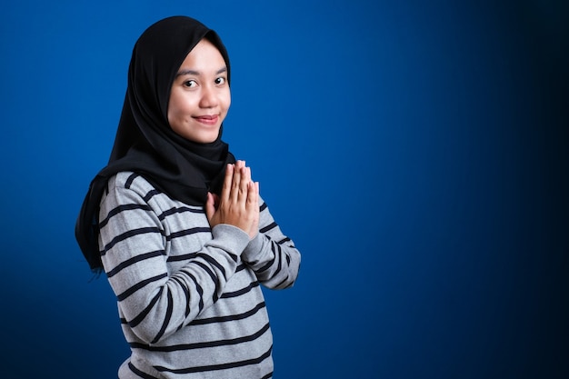 青い背景にゲストのジェスチャーを歓迎するアジアのイスラム教徒の女性