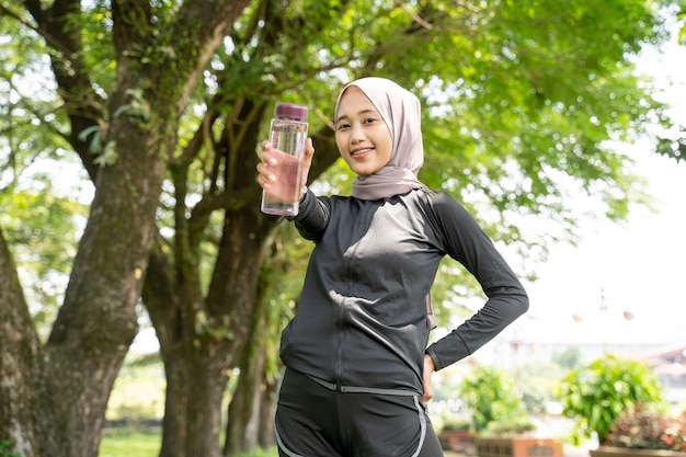 Donna musulmana asiatica con foulard che beve una bottiglia d'acqua durante l'esercizio all'aperto