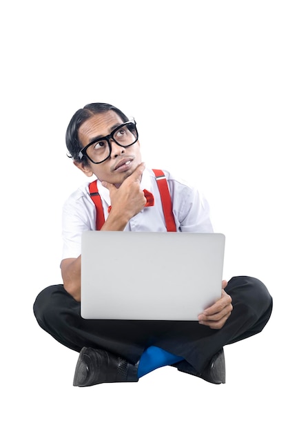 Asian nerd with ugly face sitting while using a laptop and thinking something isolated over white background