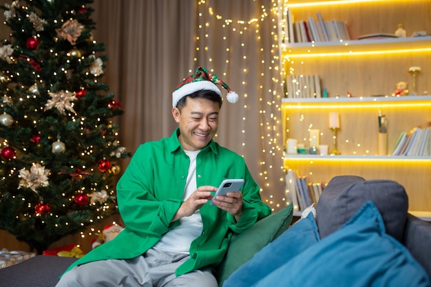 Asian new years hat uses the phone smiles reads good news smartphone in a green shirt sits on the