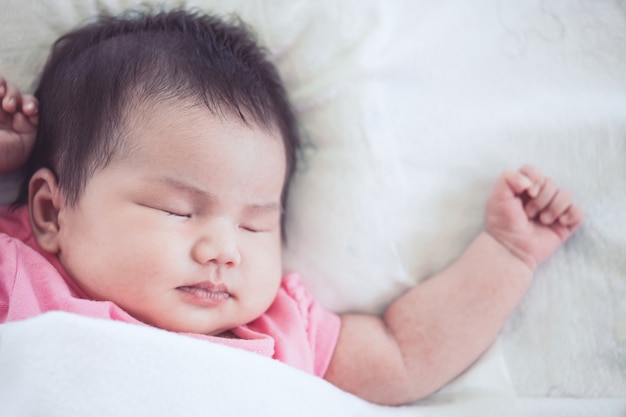 Asian newborn baby girl sleeping on white bed