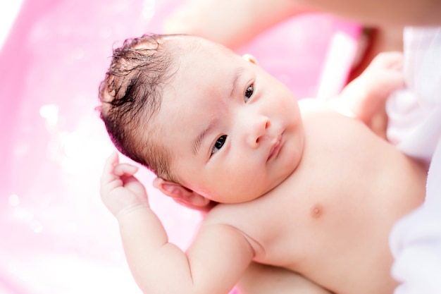 Asian newborn having a bath in ping basin by new mother