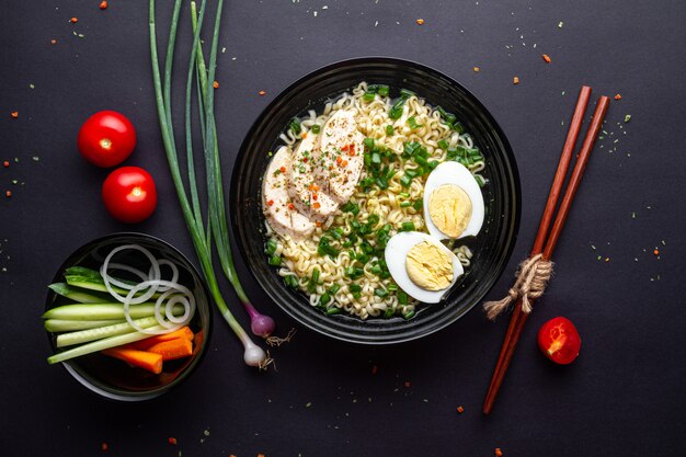 Asian noodle soup. Ramen with chicken, vegetables and egg in black bowl. Top view.