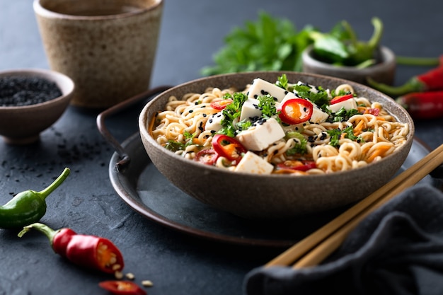 Zuppa di noodle asiatica, ramen con tofu e verdure in una ciotola di ceramica su sfondo scuro, fuoco selettivo