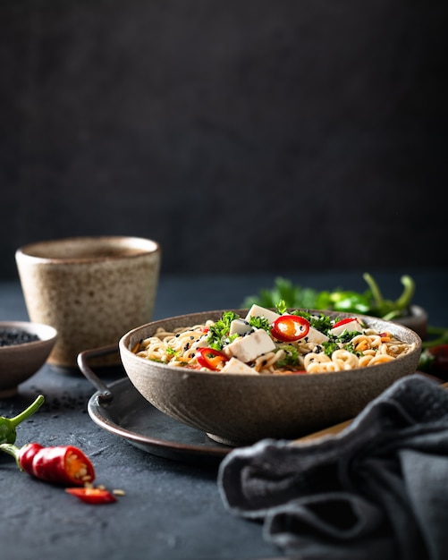 Asian noodle soup, ramen with tofu and vegetables in ceramic bowl on dark background, selective