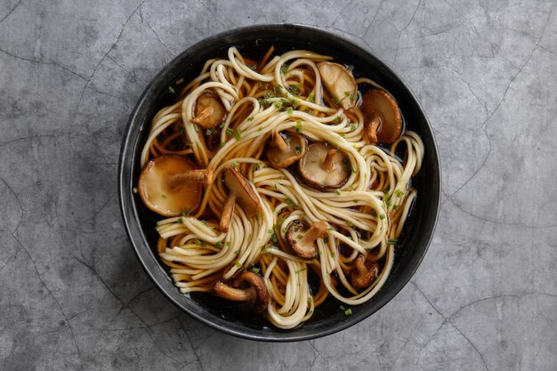 Asian noodles soup with mushrooms shiitake served in dark bowl. Closeup