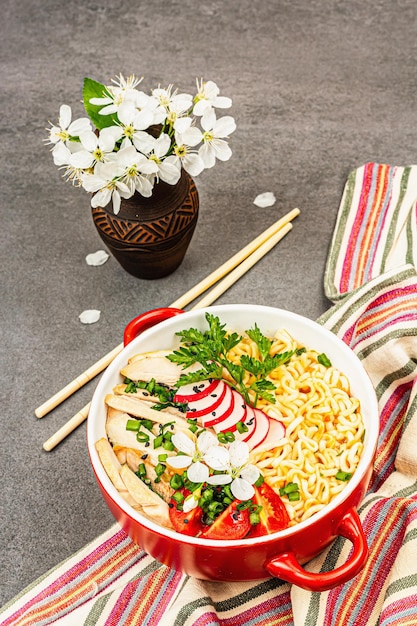 Asian noodles with chicken vegetables and herbs in a red bowl Traditional Japanese soup