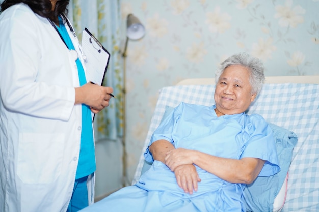 Asian nurse physiotherapist doctor talk with senior woman patient at hospital.