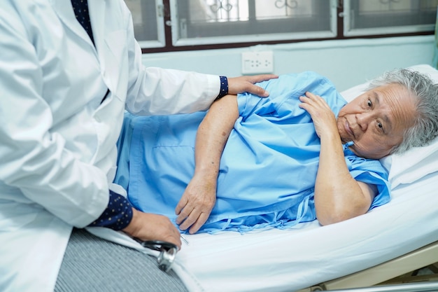 Fisioterapista asiatico dell'infermiera che tocca vecchio paziente con amore e cura.