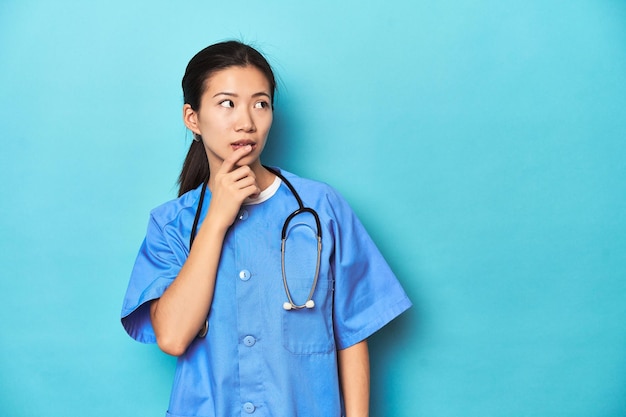Азиатская медсестра со стетоскопом в медицинской студии снята расслабленно, думая о чем-то смотрящем