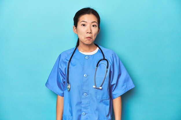 Asian nurse with stethoscope medical studio shot shrugs shoulders and open eyes confused