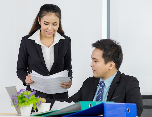 Asian office people are secretary smiling and holding document paper for presentation to boss manager while sitting and looking paper document on her hand in office place.